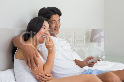 Smiling asian couple lying on bed watching tv