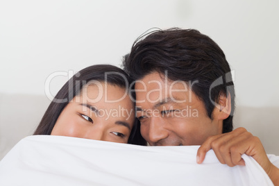 Happy couple holding duvet over face