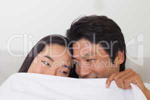 Happy couple holding duvet over face