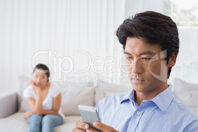 Man sending a text while girlfriend watches from couch