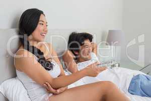 Smiling asian couple lying on bed watching tv