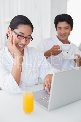 Couple in bathrobes spending the morning together using laptop