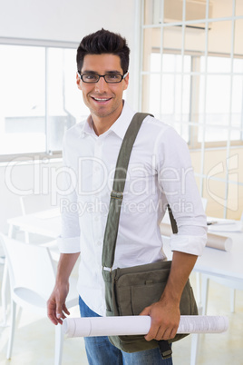 Casual handsome architect smiling at camera holding blueprint