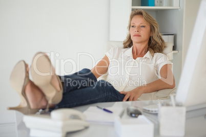 Casual businesswoman sitting at her desk with feet up