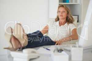 Casual businesswoman sitting at her desk with feet up