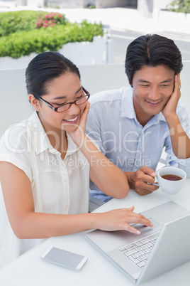 Smiling couple having breakfast together using laptop