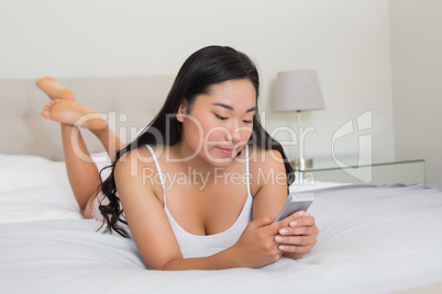 Happy woman lying on bed holding smartphone