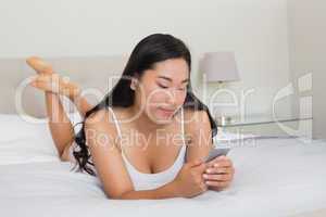 Happy woman lying on bed holding smartphone