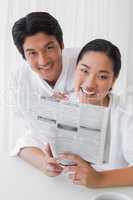 Couple in bathrobes reading newspaper together in the morning