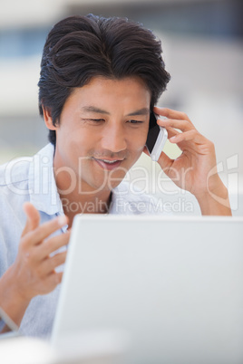 Happy man using his laptop talking on the phone