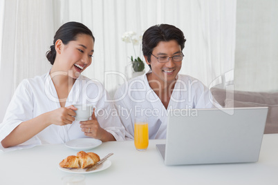 Happy couple using laptop over breakfast