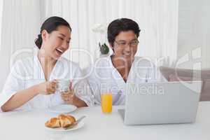 Happy couple using laptop over breakfast