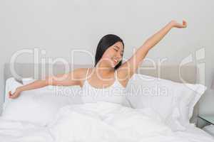 Smiling woman stretching in bed in the morning