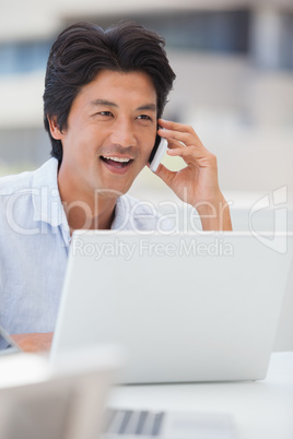 Happy man using his laptop talking on the phone