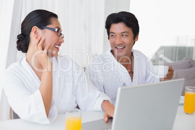 Couple in bathrobes spending the morning together using laptop