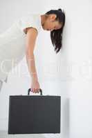 Casual businesswoman leaning against wall with briefcase