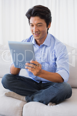 Happy man sitting on couch using tablet pc