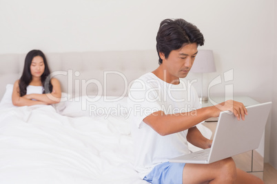 Woman watching boyfriend using laptop on end of bed