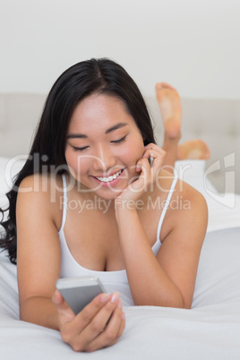 Happy woman lying on bed holding smartphone