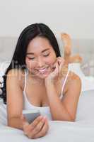 Happy woman lying on bed holding smartphone