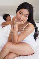 Woman sitting on end of bed as boyfriend sleeps