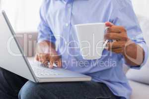 Man sitting on couch using laptop having coffee