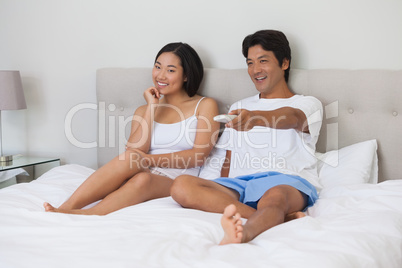 Happy couple lying on bed together watching tv