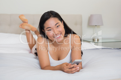 Happy woman lying on bed holding smartphone