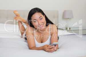 Happy woman lying on bed holding smartphone