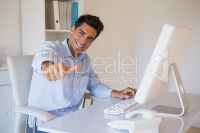 Casual businessman giving thumbs up to camera at his desk