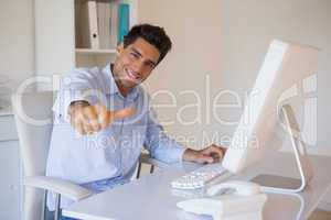 Casual businessman giving thumbs up to camera at his desk