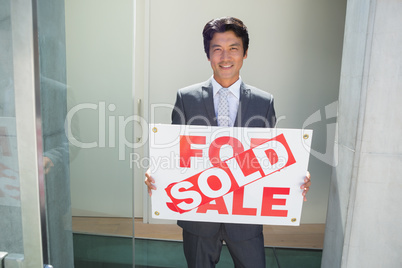 Confident estate agent standing at front door showing sold sign