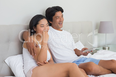 Smiling asian couple lying on bed watching tv