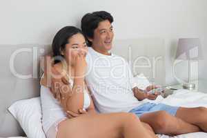 Smiling asian couple lying on bed watching tv