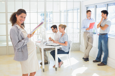 Pregnant businesswoman smiling at camera with team behind her