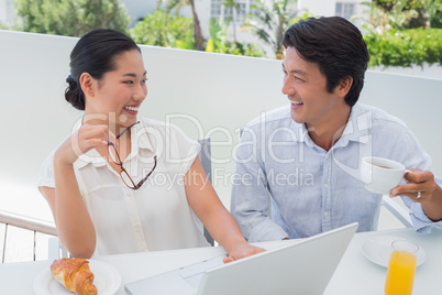 Smiling couple having breakfast together using laptop