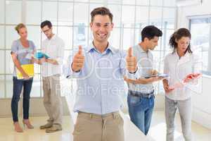 Casual boss giving thumbs up at camera in front of business team