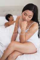 Woman sitting on end of bed as boyfriend sleeps