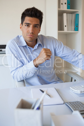 Casual businessman frowning at camera at his desk