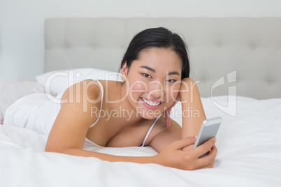 Smiling asian woman lying on bed sending a text