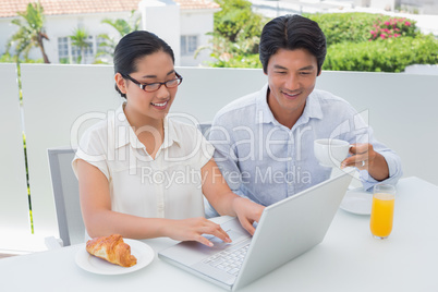 Smiling couple having breakfast together using laptop