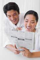 Couple in bathrobes reading newspaper together in the morning