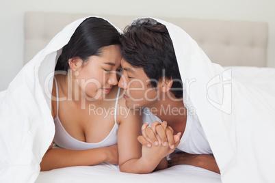 Happy couple lying on bed together under the duvet