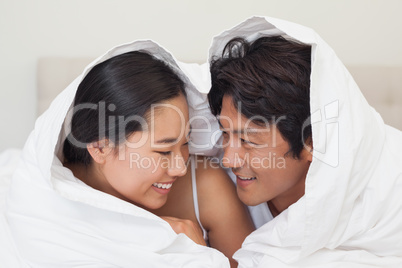 Happy couple lying on bed together under the duvet