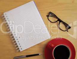 Overhead of notebook and glasses with pen and coffee cup