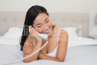 Happy woman lying on bed talking on the land line