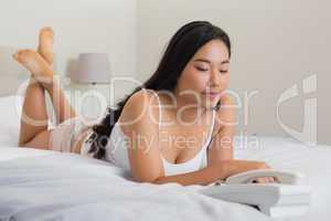 Happy woman lying on bed holding telephone