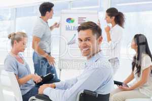 Casual businessman in wheelchair smiling at camera during presen