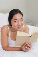 Smiling woman lying on bed reading