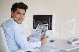 Casual businessman reading newspaper at his desk